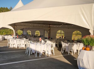 White chairs and round tables set up under outdoor marquis tent for a wedding